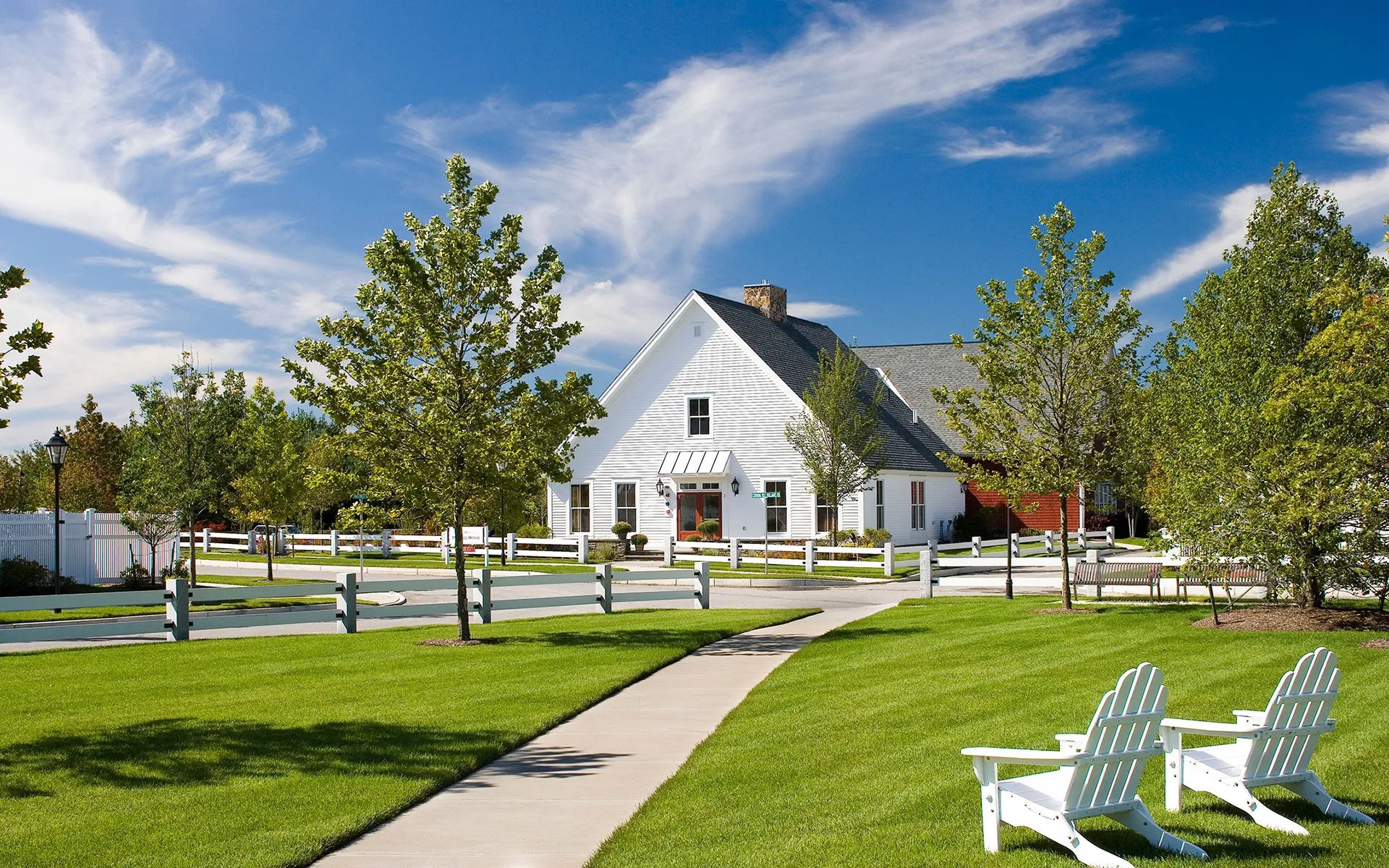 Clubhouse and village green at Red Mill Village 55+ community in Norton MA with white Adirondack chairs and walking path