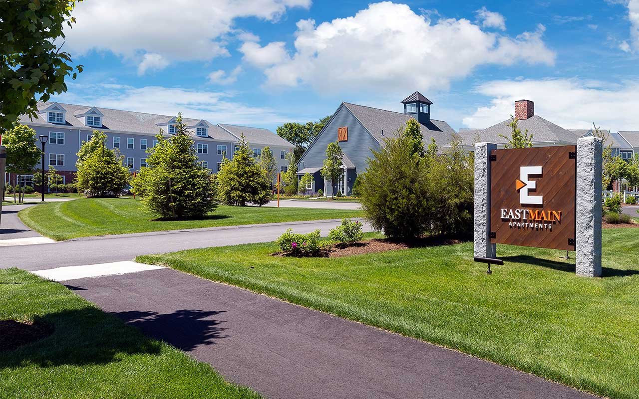 Entry drive and central green at EastMain Apartments in Norton MA, with the barn-style clubhouse in the background