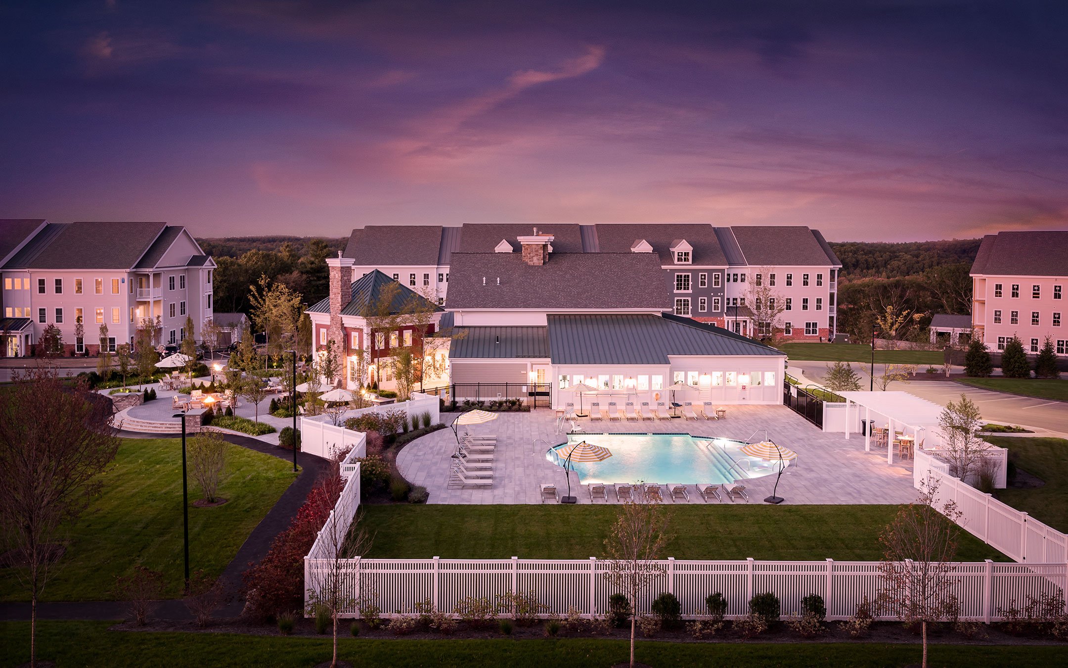 Aerial dusk view of Cirrus apartments in Ashland MA showing illuminated clubhouse, pool, and courtyard