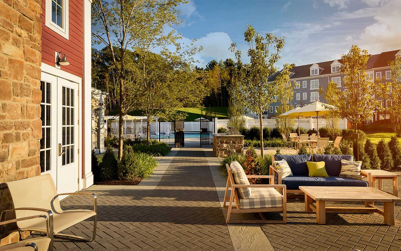 Outdoor patio and pool courtyard at Cirrus apartments in Ashland MA with teak seating, brick pavers, and professional landscaping