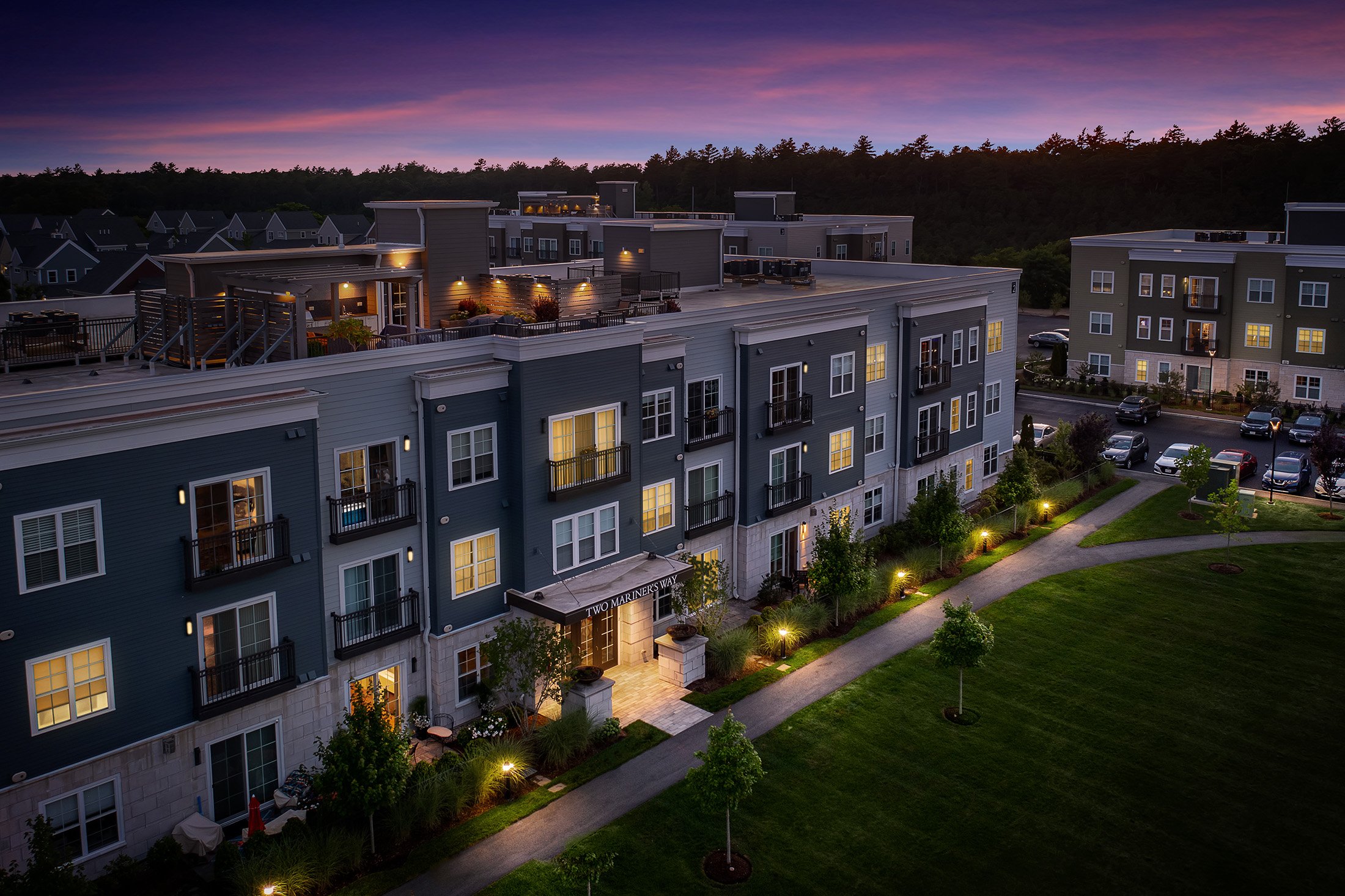 Aerial dusk view of Two Mariners Way at Sawyer's Reach in Plymouth MA with rooftop decks, balconies, and illuminated entry