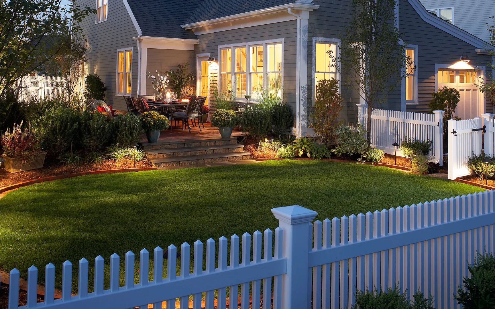 Home with landscape lighting and white picket fence at Red Mill Village in Norton MA